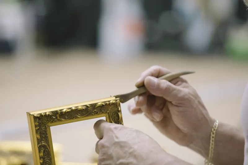A framer filling the corner of a gilded frame by hand.